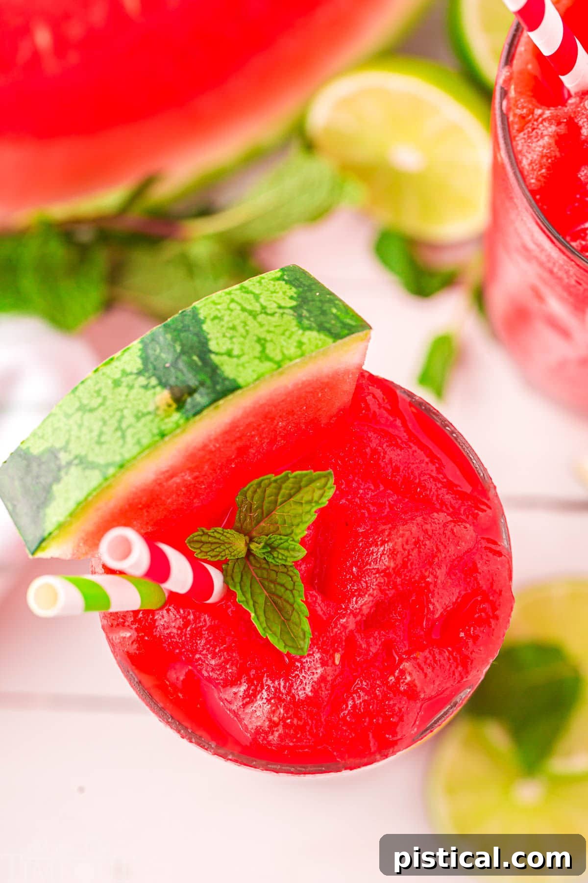 A top-down view of a glass of watermelon slushie, positioned next to a halved watermelon, highlighting the fresh ingredients.