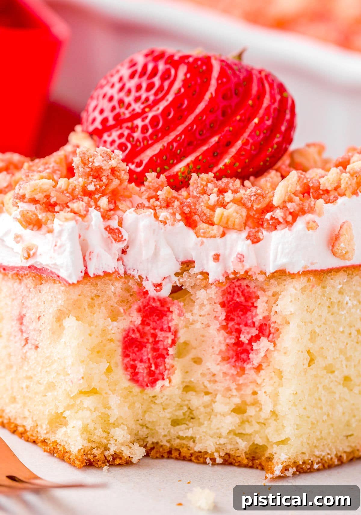 piece of strawberry crunch cake on plate with one forkful removed. close up shows the red jello that has been added to the poke cake.