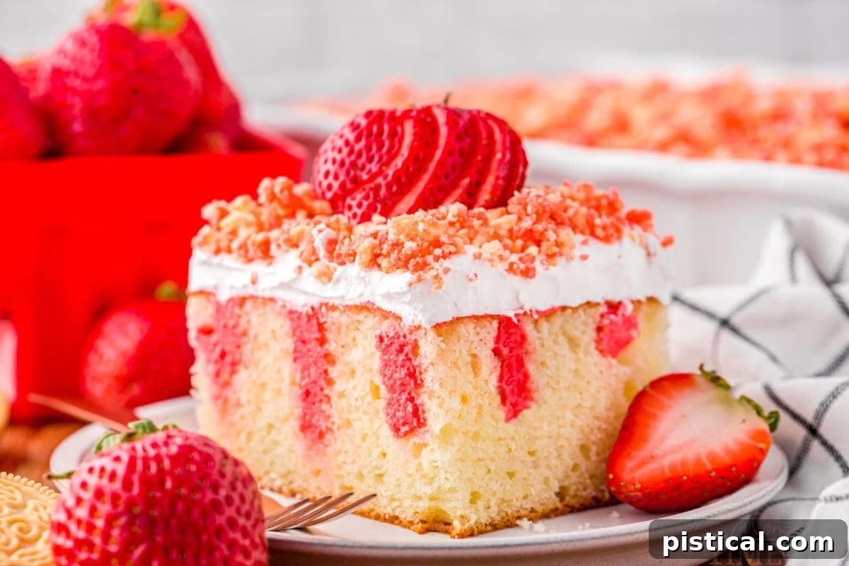 serving of strawberry poke cake on small white round plate topped with fresh sliced strawberry and crunch topping. rest of cake can be seen in background.