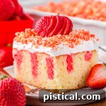 serving of strawberry poke cake on small white round plate topped with fresh sliced strawberry and crunch topping. rest of cake can be seen in background.