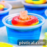 blue pool party jello shot with gummi bear sitting on white surface. more jello shots can be seen in the background.