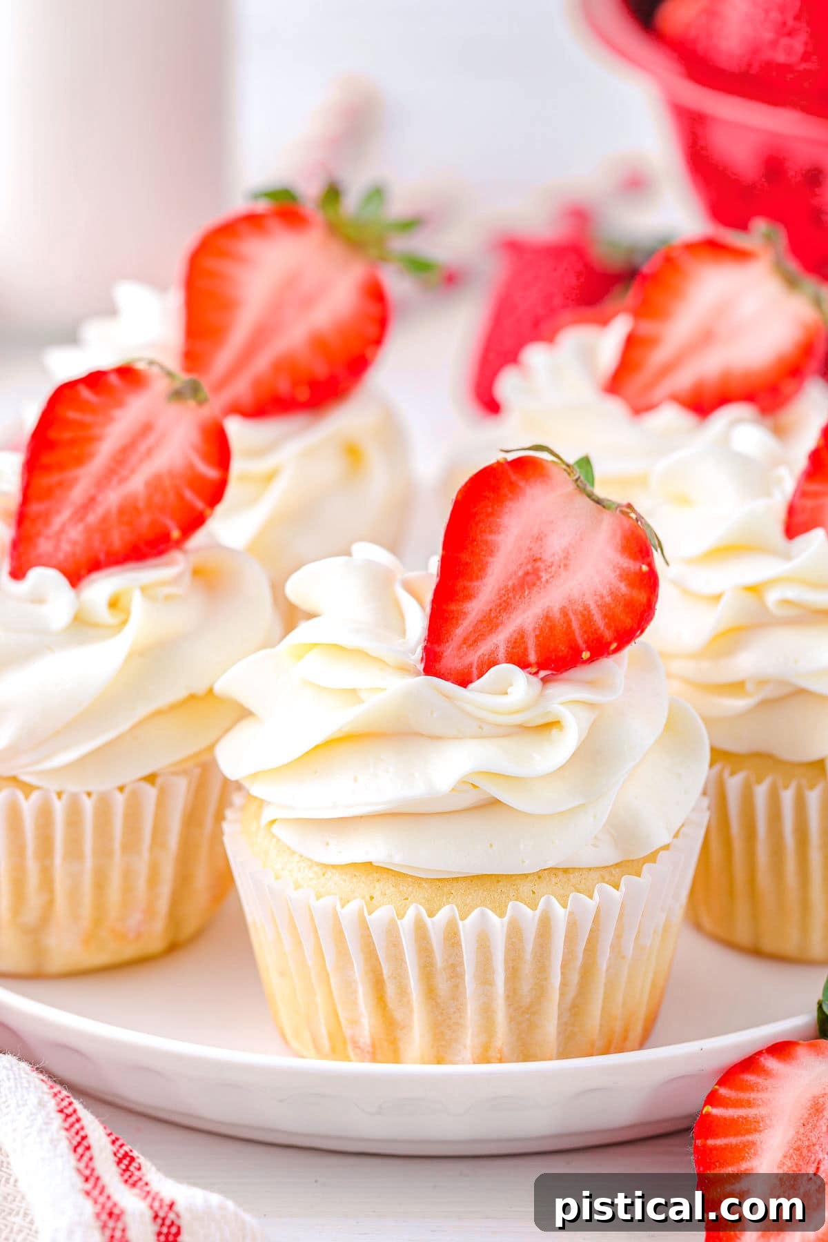 Five strawberry shortcake cupcakes arranged on a white plate, each topped with a fresh strawberry half and luscious buttercream frosting.