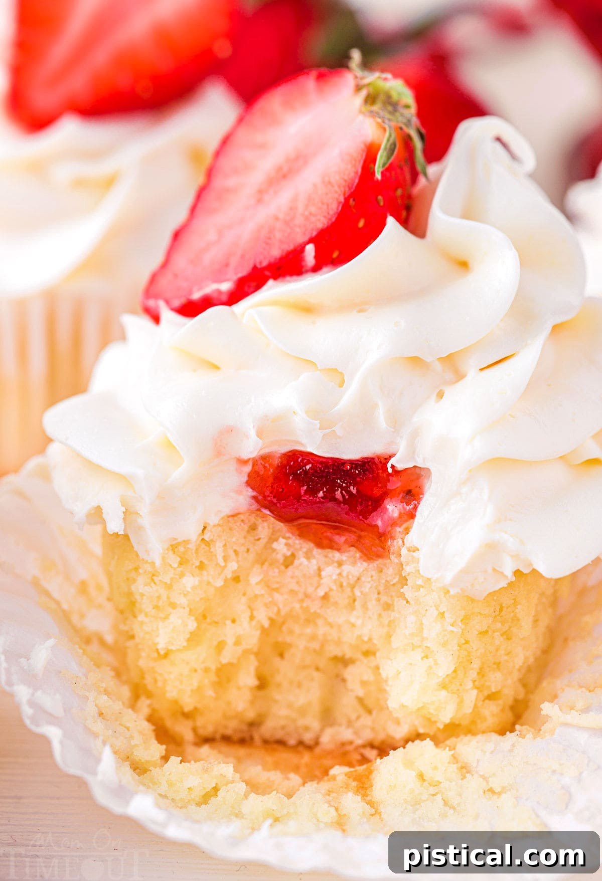 Close-up view of a strawberry shortcake cupcake revealing the juicy strawberry jam filling inside, topped with fluffy vanilla buttercream frosting.