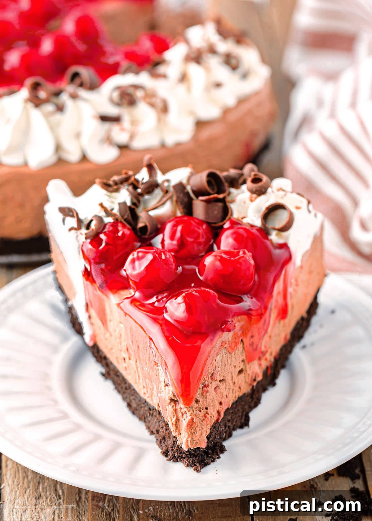 Slice of no bake black forest cheesecake on white round plate, showcasing the chocolate cheesecake layer, Oreo crust, and cherry topping with whipped cream.