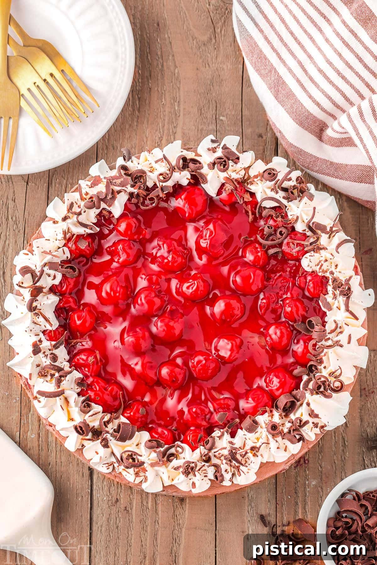 Top down view of whole no bake black forest cheesecake sitting on wood board, beautifully garnished with whipped cream, cherry pie filling, and chocolate shavings.