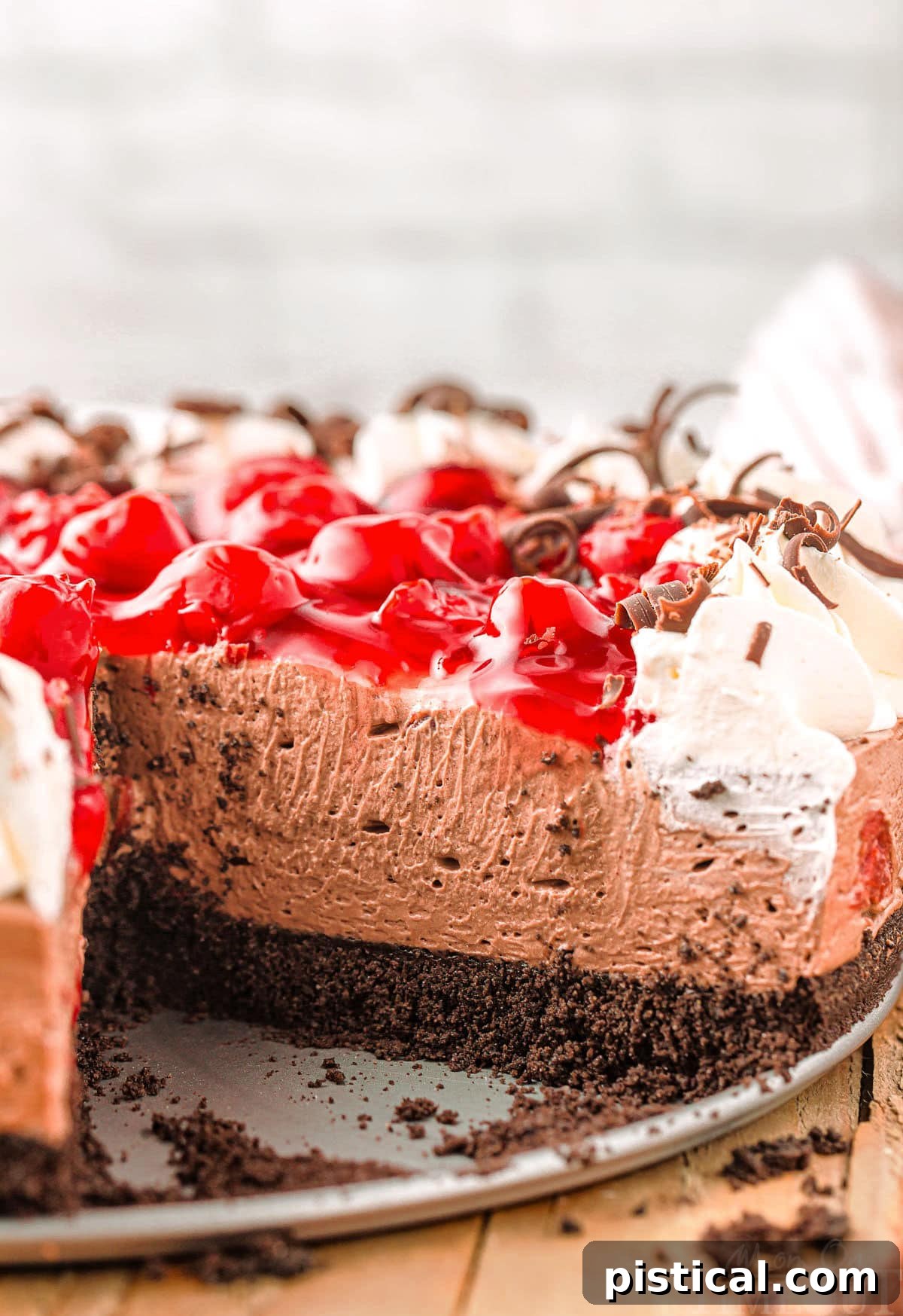 Cross section of no bake black forest cheesecake showing creamy chocolate cheesecake and cherry pie filling topping along with whipped cream and chocolate shavings.