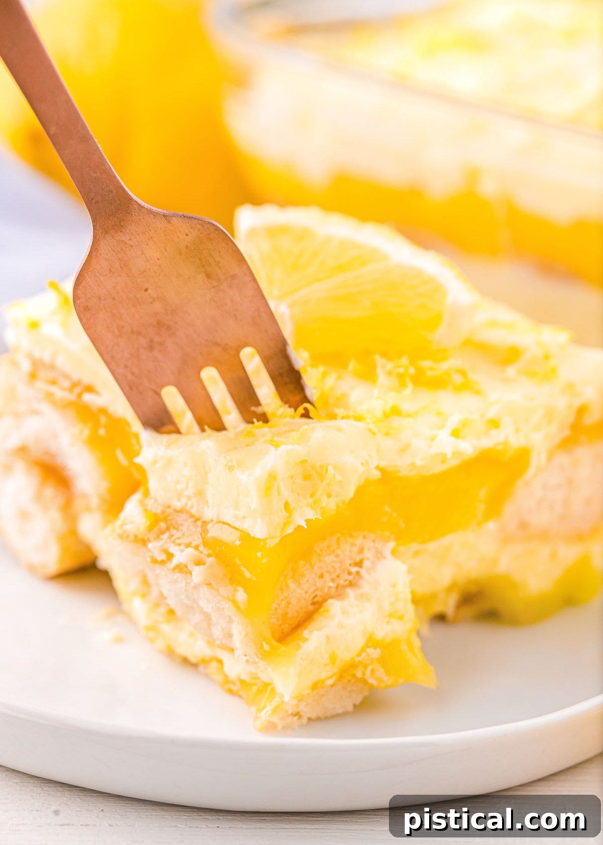 A forkful of bright lemon tiramisu is gently lifted away from a round white plate, showcasing the dessert's delightful texture and inviting appearance.