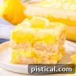 layered lemon tiramisu dessert cut into a square on a white dessert plate with the rest of the dessert in the background.