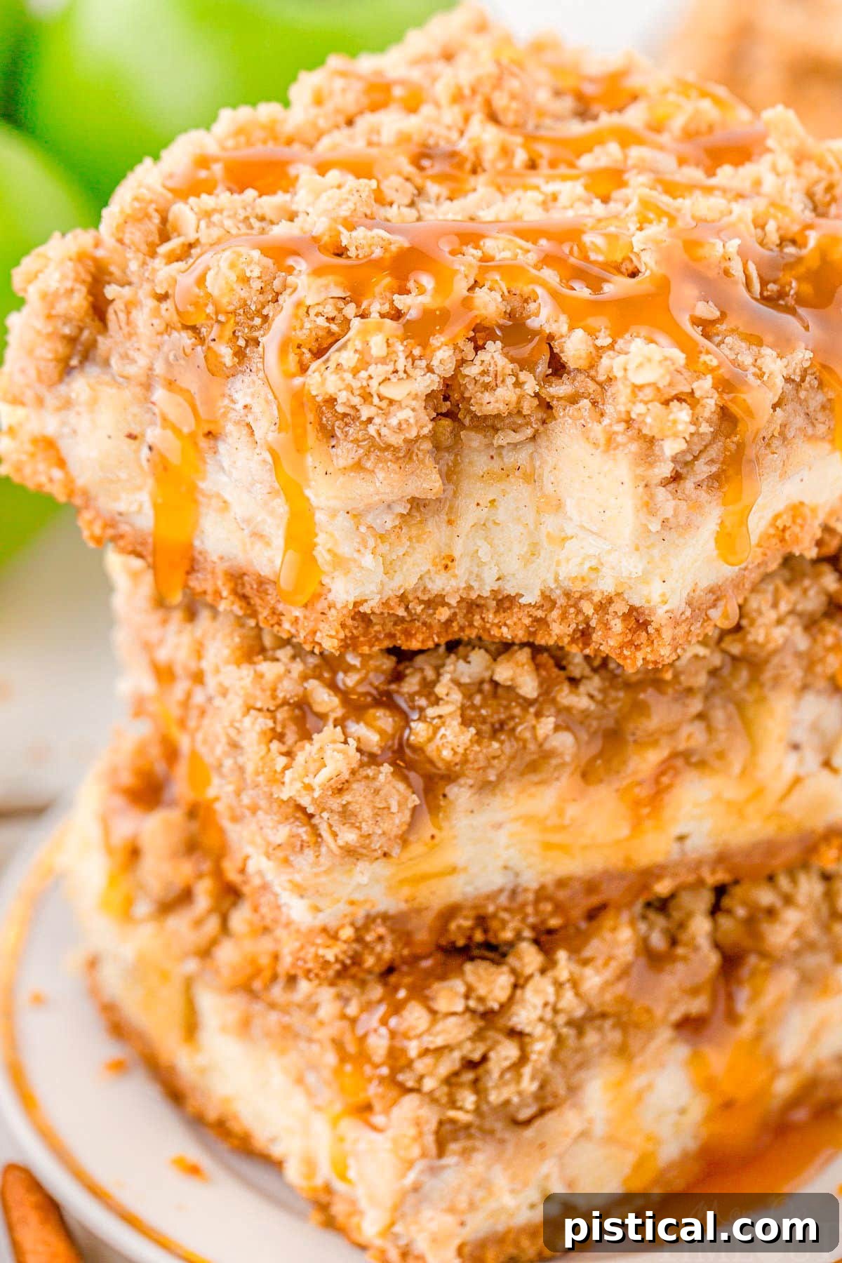 Spiced Caramel Apple Cheesecake Bars 3 Three caramel apple cheesecake bars stacked on a white plate. The top bar has a delicious bite taken out of it, revealing the distinct layers of crust, cheesecake, and spiced apples, with caramel drizzled generously on top.