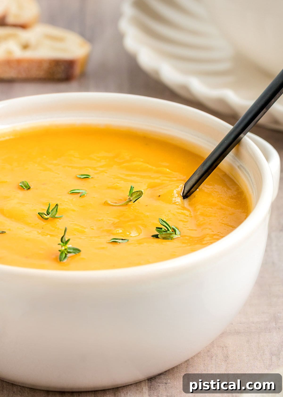 close up look at butternut squash soup with bright orange color in white bowl topped with fresh thyme.