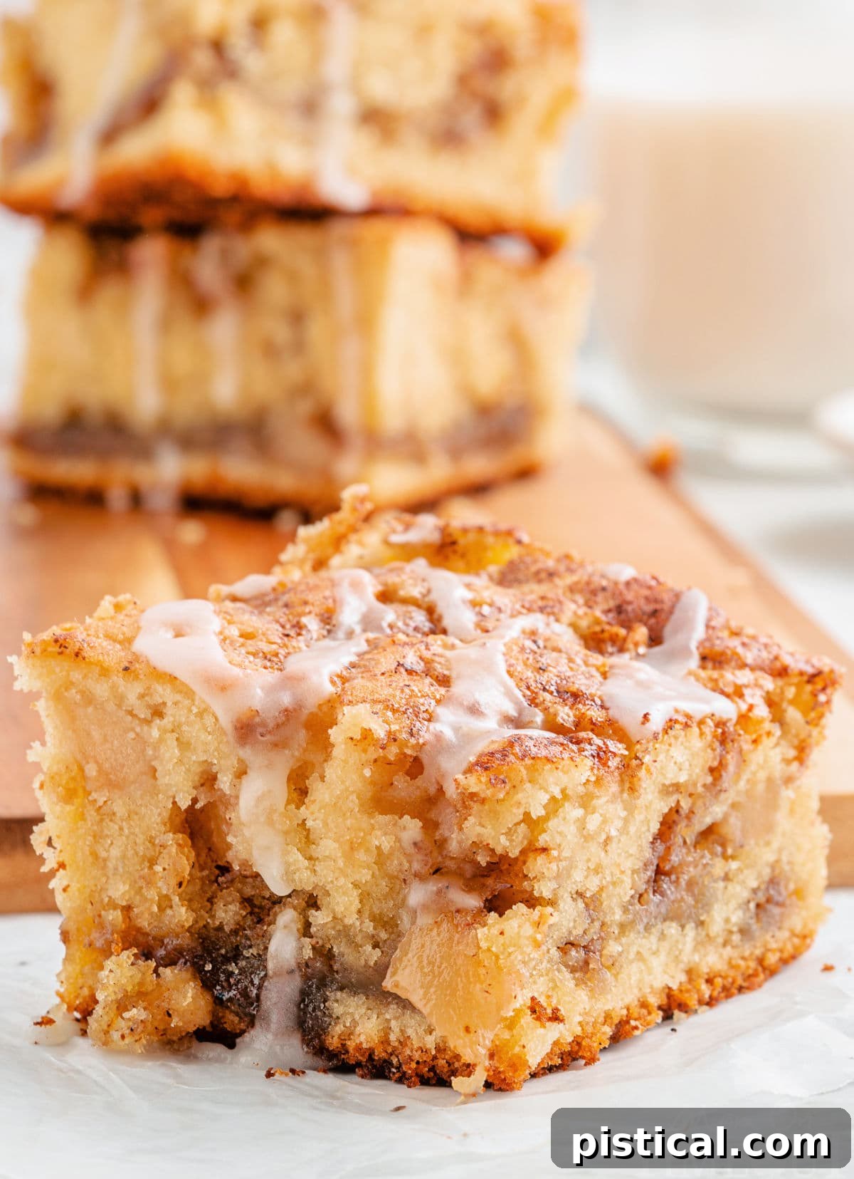 A slice of glazed apple coffee cake, rich with cinnamon and apples, rests on a marble board, ready to be enjoyed.