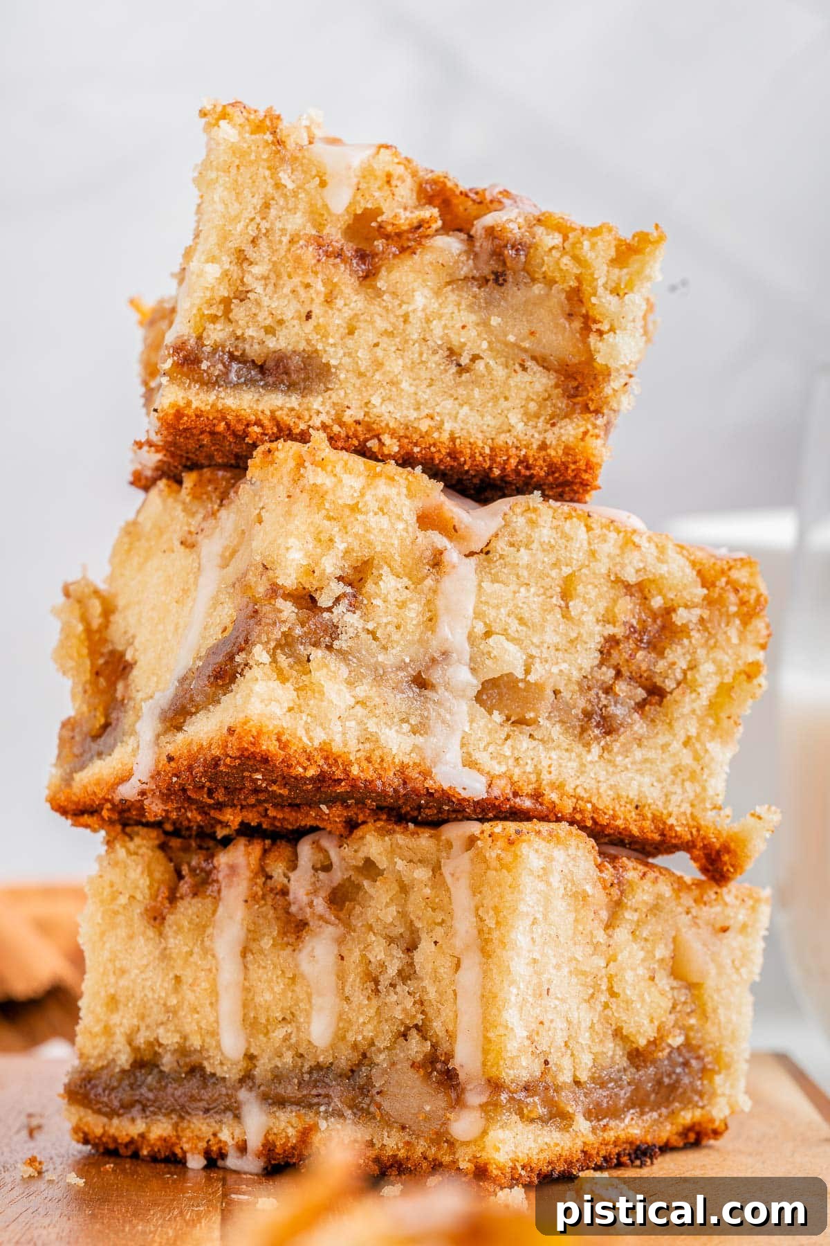 Three pieces of apple coffee cake, generously drizzled with glaze, stacked on a rustic wooden cutting board, highlighting the moist interior.