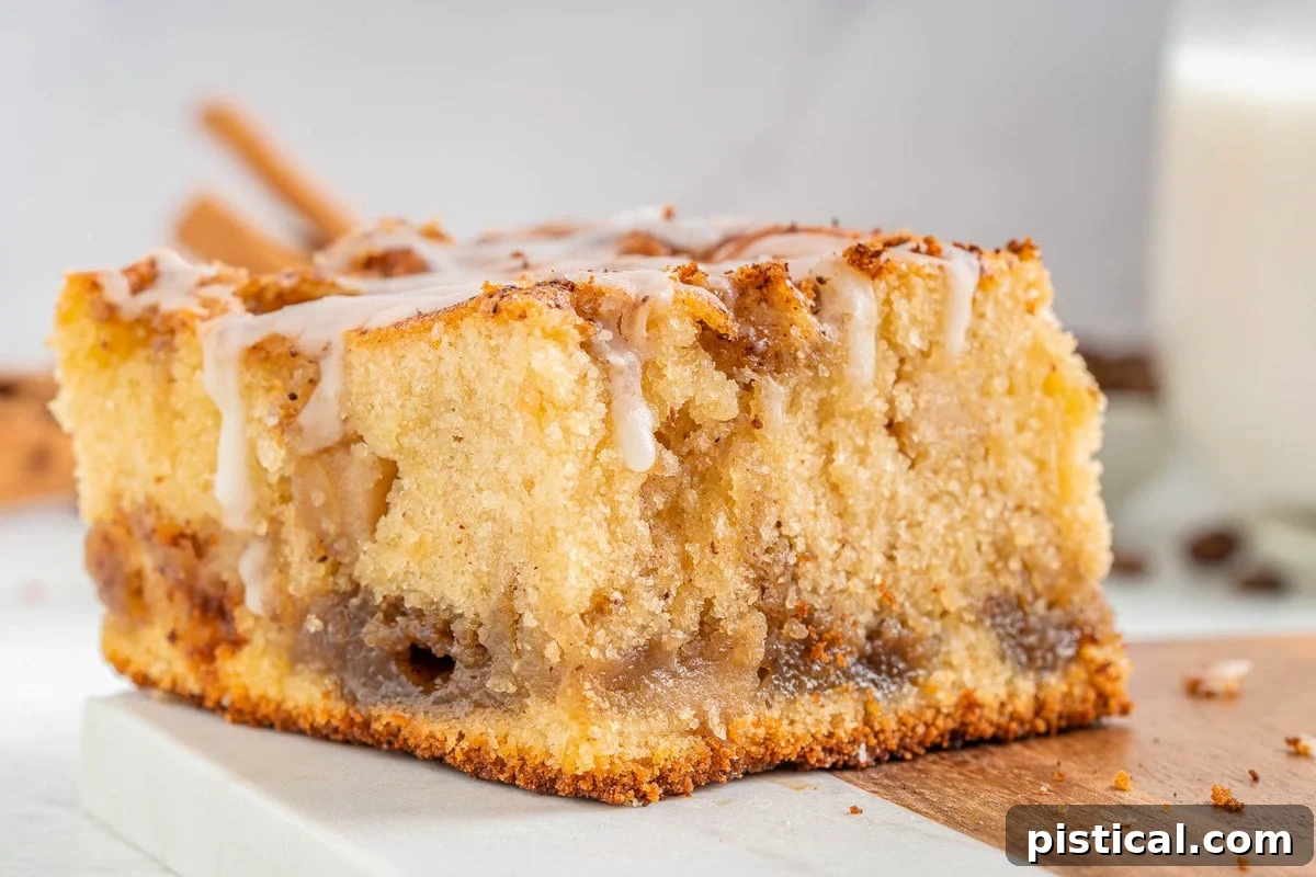 A single piece of glazed apple coffee cake with a rich, moist crumb on a marble and wood cutting board, showcasing its autumnal appeal.