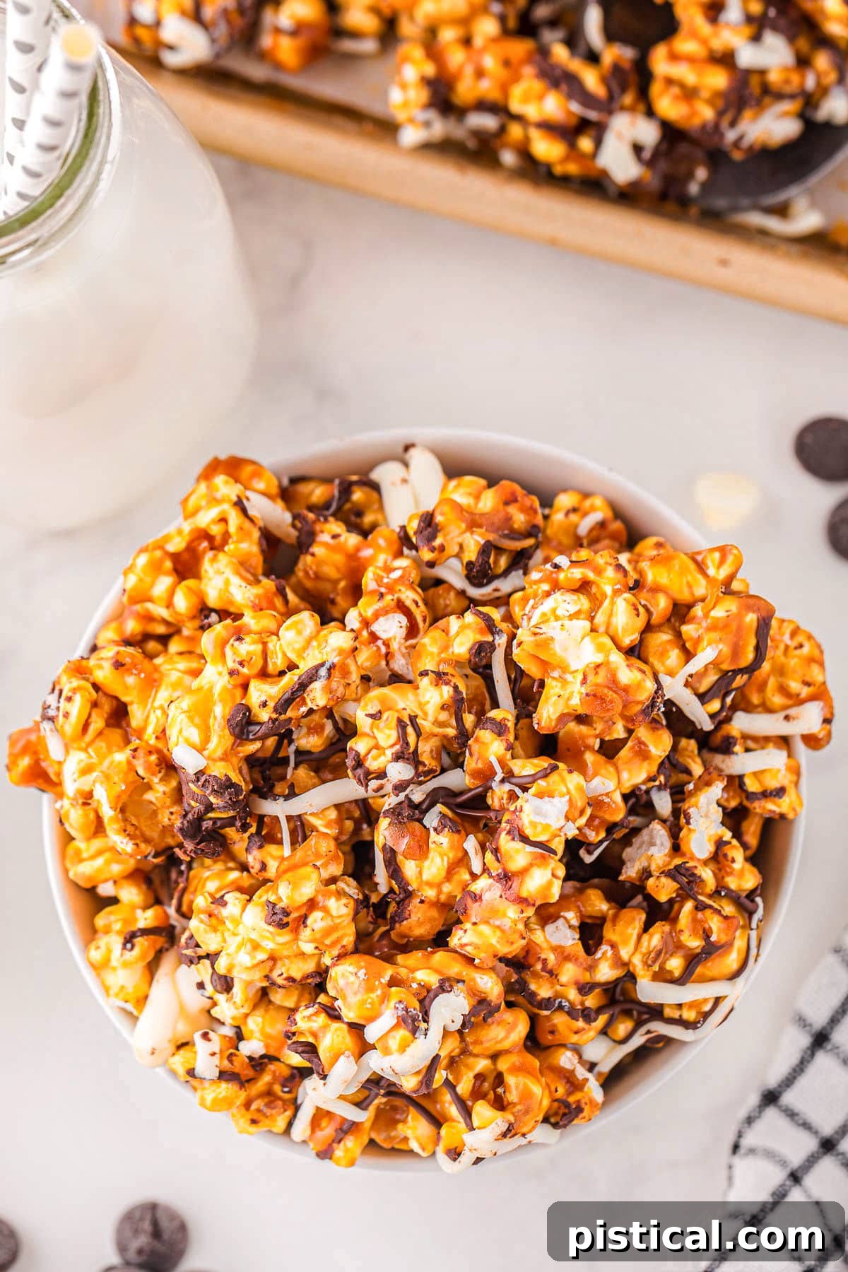 top down look at caramel corn in white bowl on marble surface. popcorn has been drizzled with white and dark chocolate.