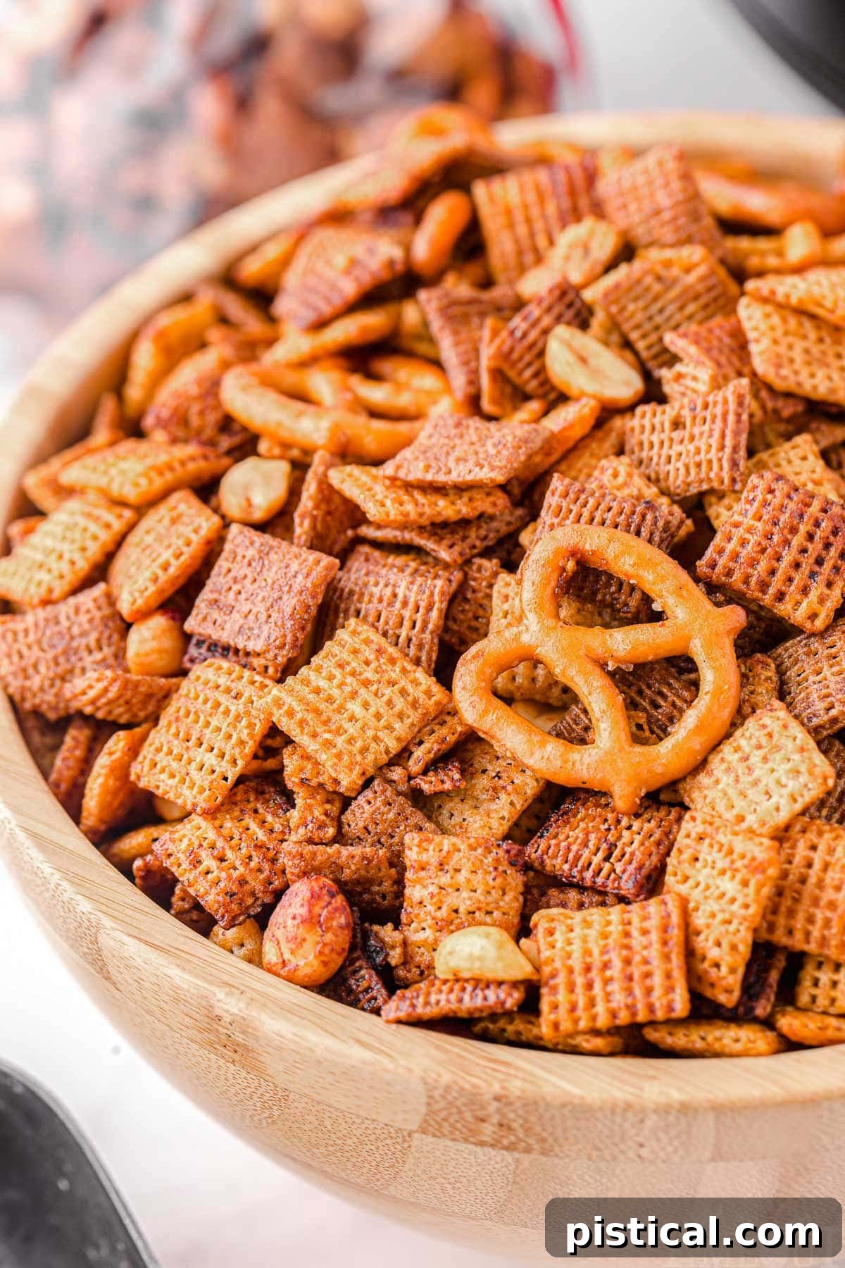 Close-up view of irresistible slow cooker Chex Mix in a large wooden bowl, highlighting its crispy texture and rich coating.