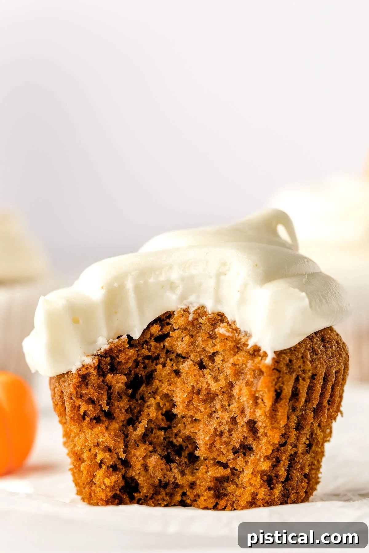 Decadent Pumpkin Cupcakes with Silky Cream Cheese Frosting 2 A single, perfectly frosted pumpkin cupcake on a white liner, with a bite taken out to reveal its tender, moist interior. The cream cheese frosting is piped high.