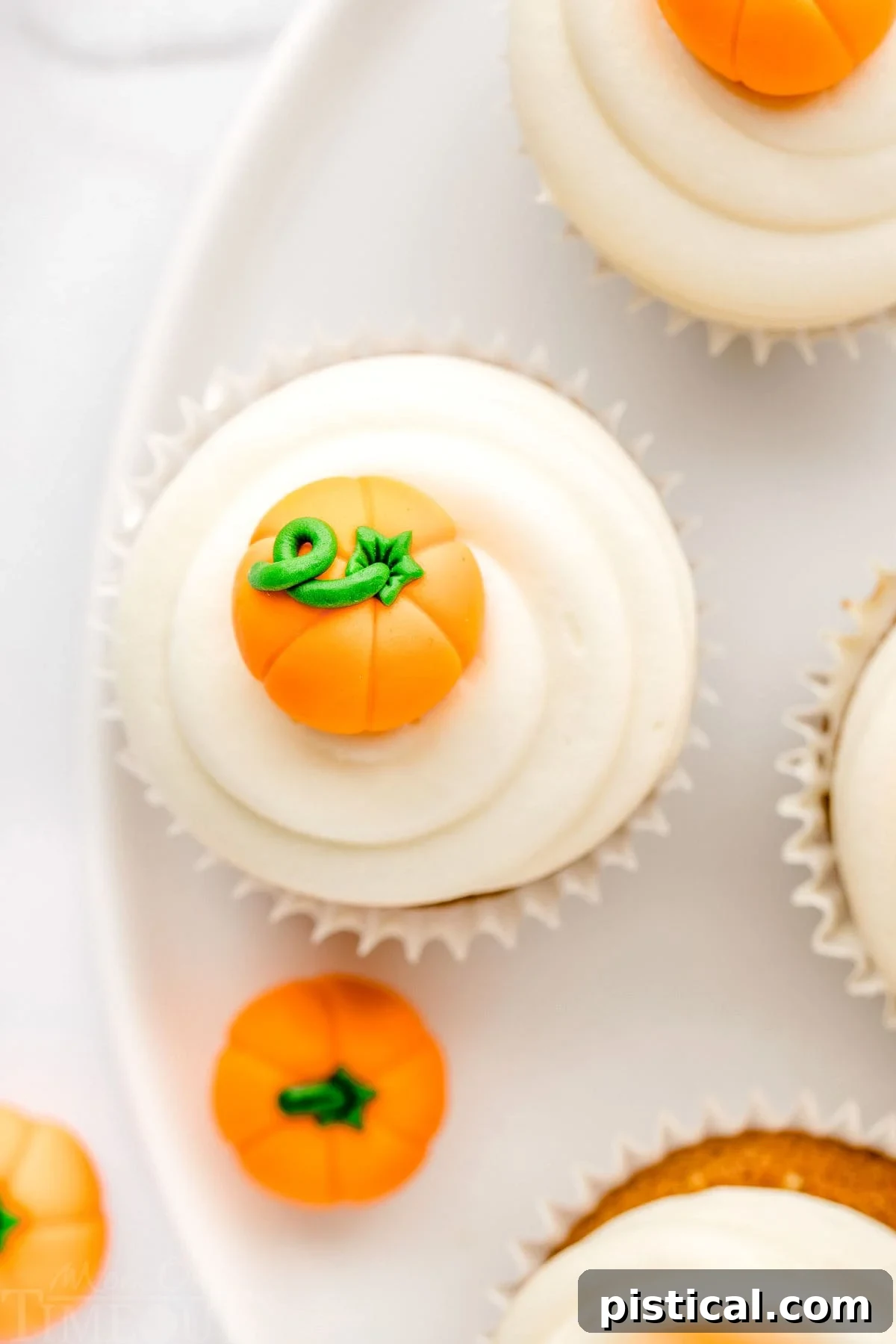 Decadent Pumpkin Cupcakes with Silky Cream Cheese Frosting 4 A top-down view of pumpkin cupcakes on a white plate, beautifully topped with swirled cream cheese frosting and small candy pumpkins.