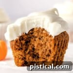 single pumpkin cupcake sitting on white cupcake liner frosted with cream cheese frosting. one large bite has been taken from the cupcake revealing a tender crumb.