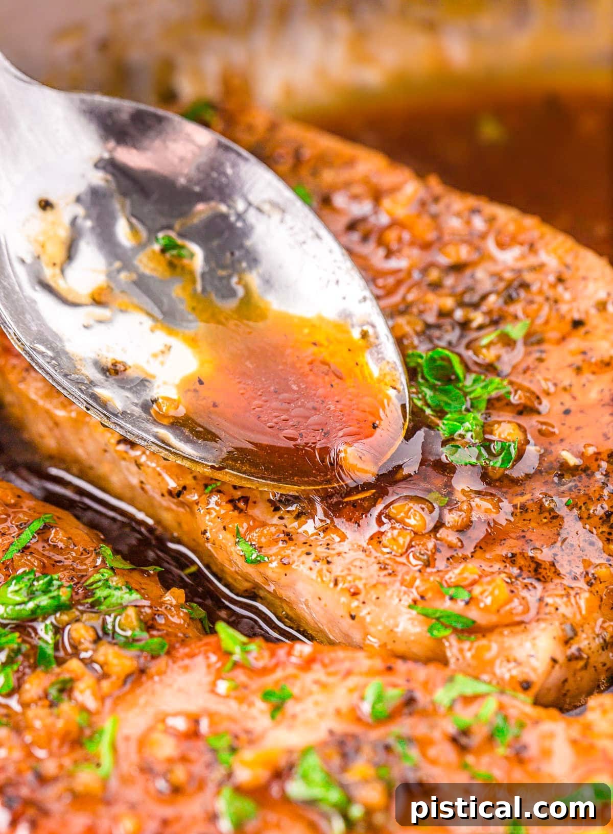 A generous spoonful of glossy honey garlic glaze being poured over a golden-brown pork chop in a hot skillet, showcasing the richness of the sauce.