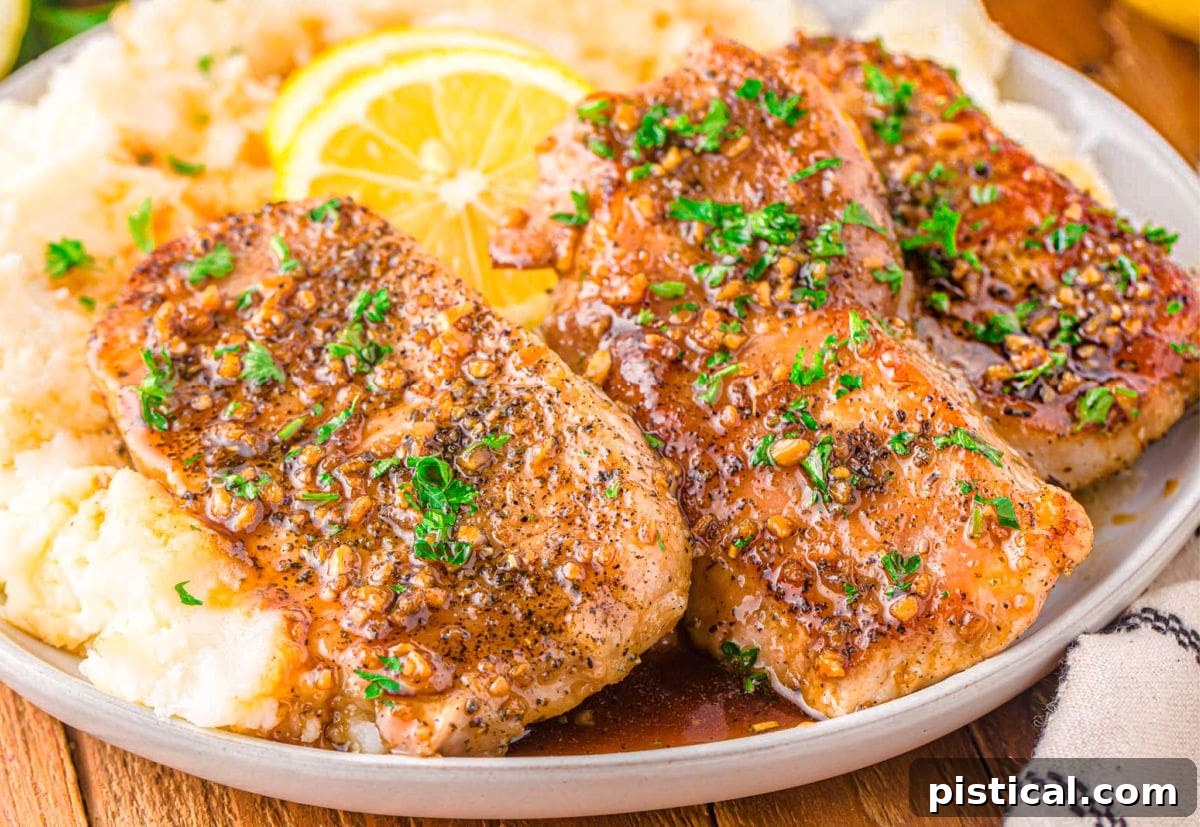 Three perfectly glazed honey garlic pork chops are arranged on a bed of fluffy mashed potatoes, elegantly garnished with fresh parsley and bright lemon slices. The entire dish rests on a warm, inviting wooden surface.