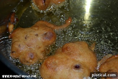 Several golden-brown cherry fritters sizzling and cooking in hot oil in a deep pan.