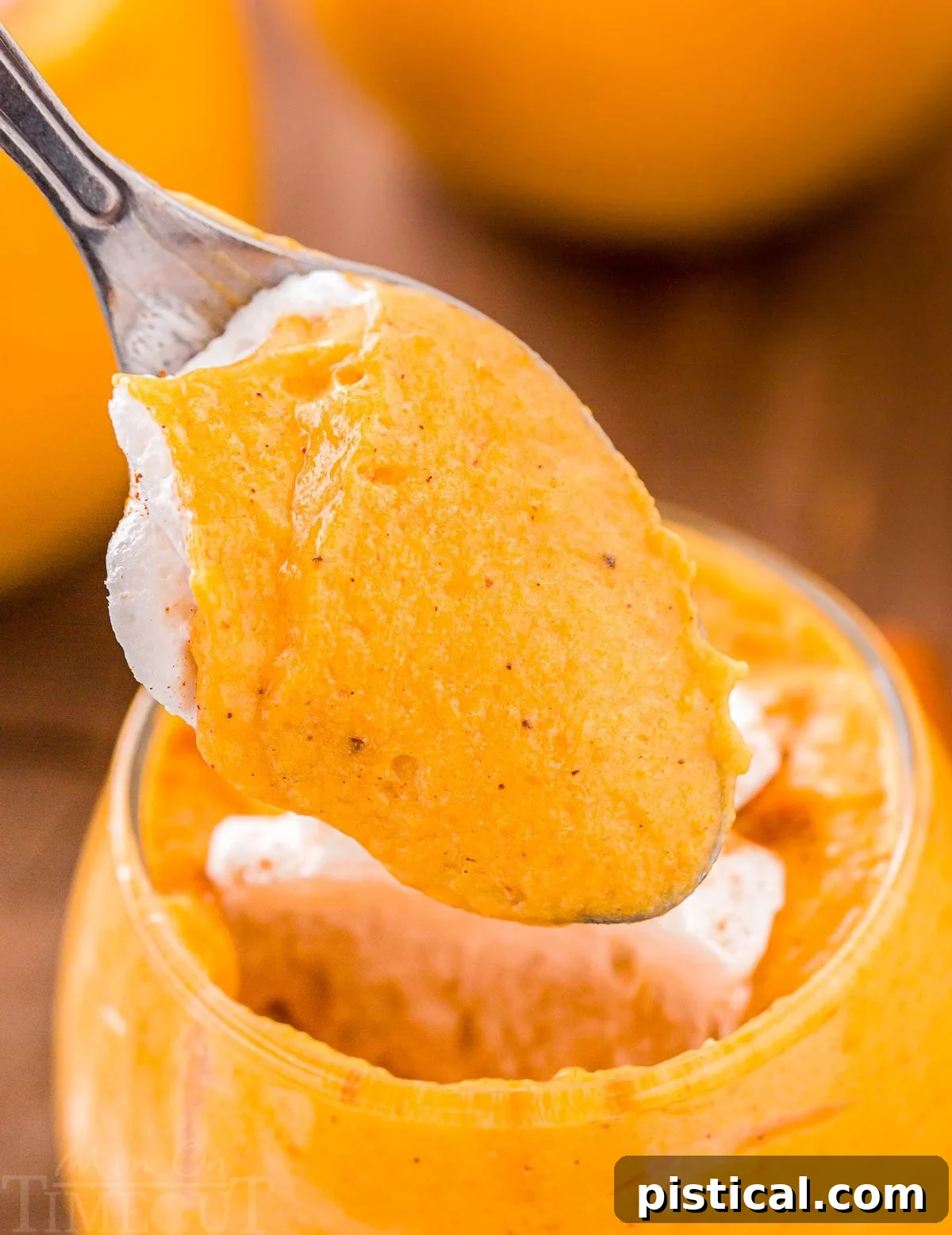 A spoonful of fluffy pumpkin mousse, adorned with whipped cream, is delicately lifted from a glass serving dish, highlighting its rich texture.