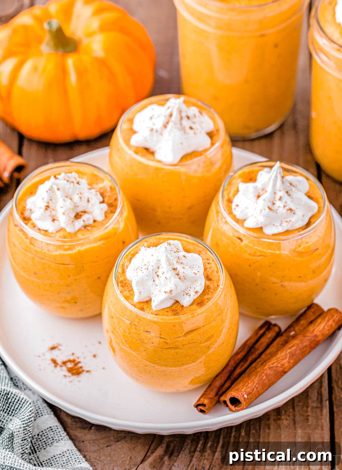 A top-down, angled view of four elegant dessert glasses, each filled with rich pumpkin mousse and topped with a generous swirl of whipped cream, beautifully garnished with pumpkin pie spice.