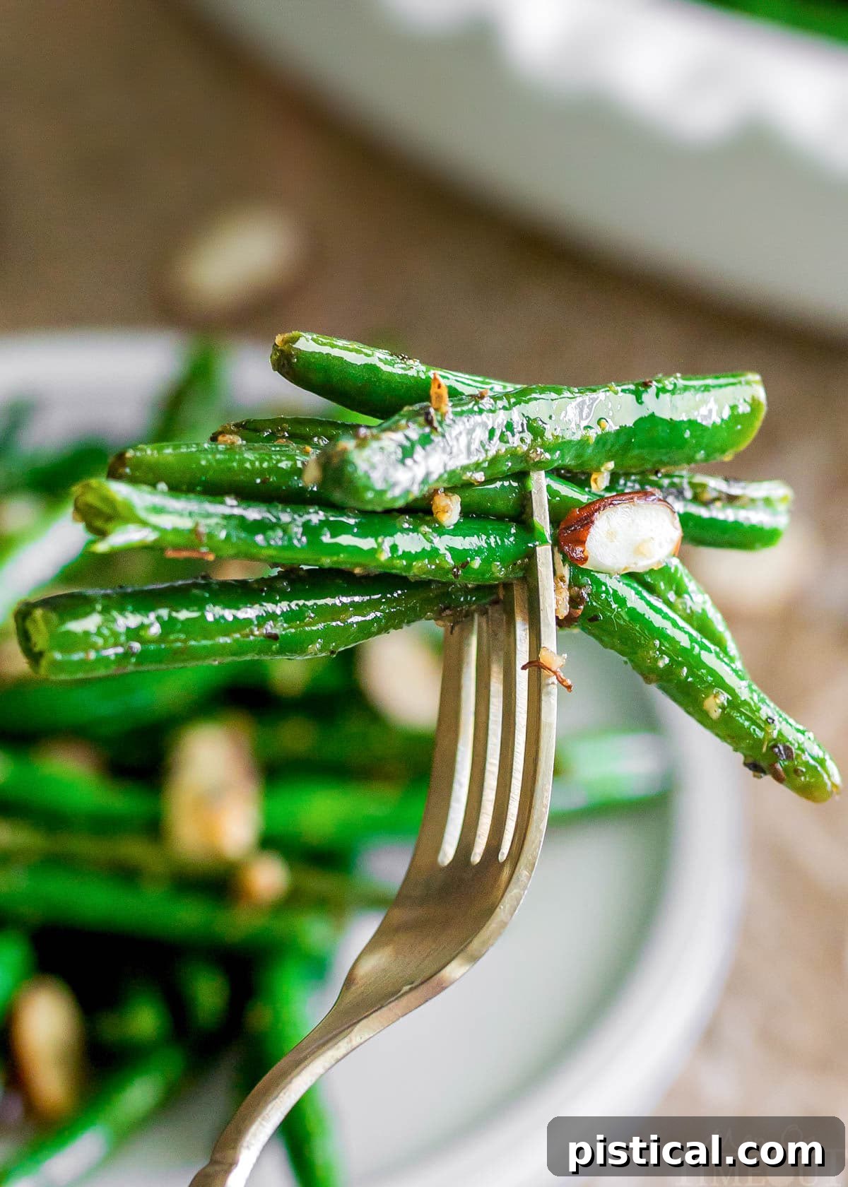A forkful of glistening brown butter garlic green beans held over a white plate, showcasing the beans' crisp texture and savory coating.