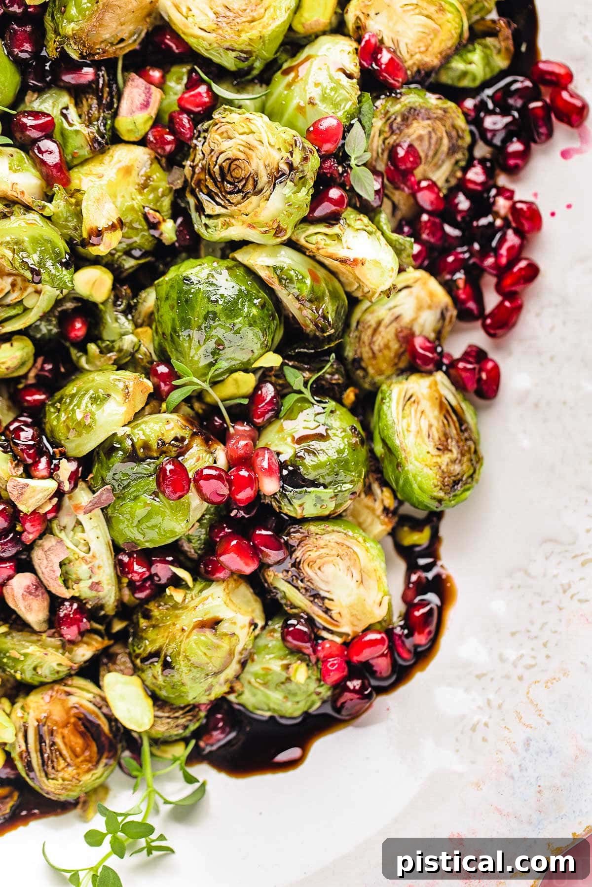 Top down view of roasted brussels sprouts on a pink and white serving dish. the sprouts are topped with pomegranate seeds and thyme along with a balsamic glaze.