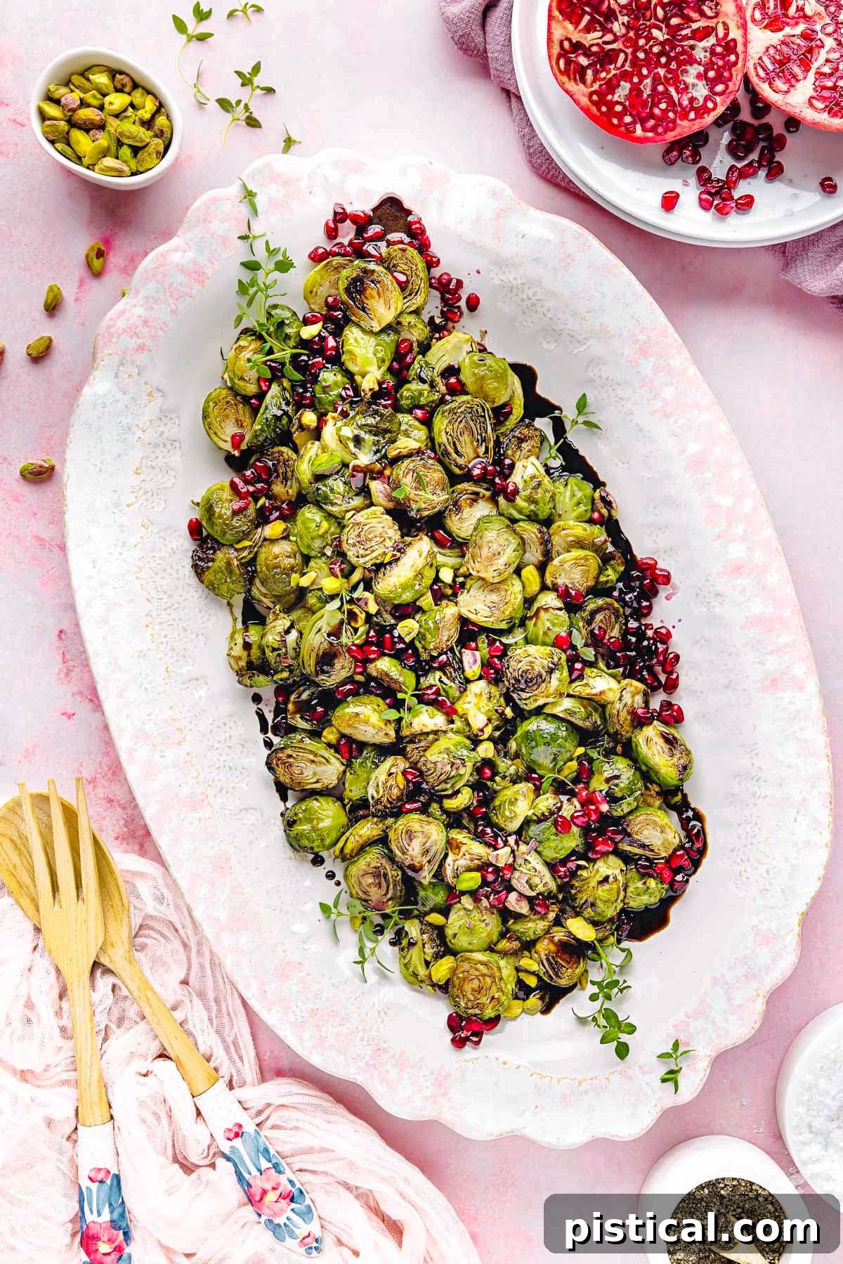 top down view of roasted brussels sprouts on a large white and pink platter. Pomegranate seeds and pistachios garnish the gorgeous dish. 