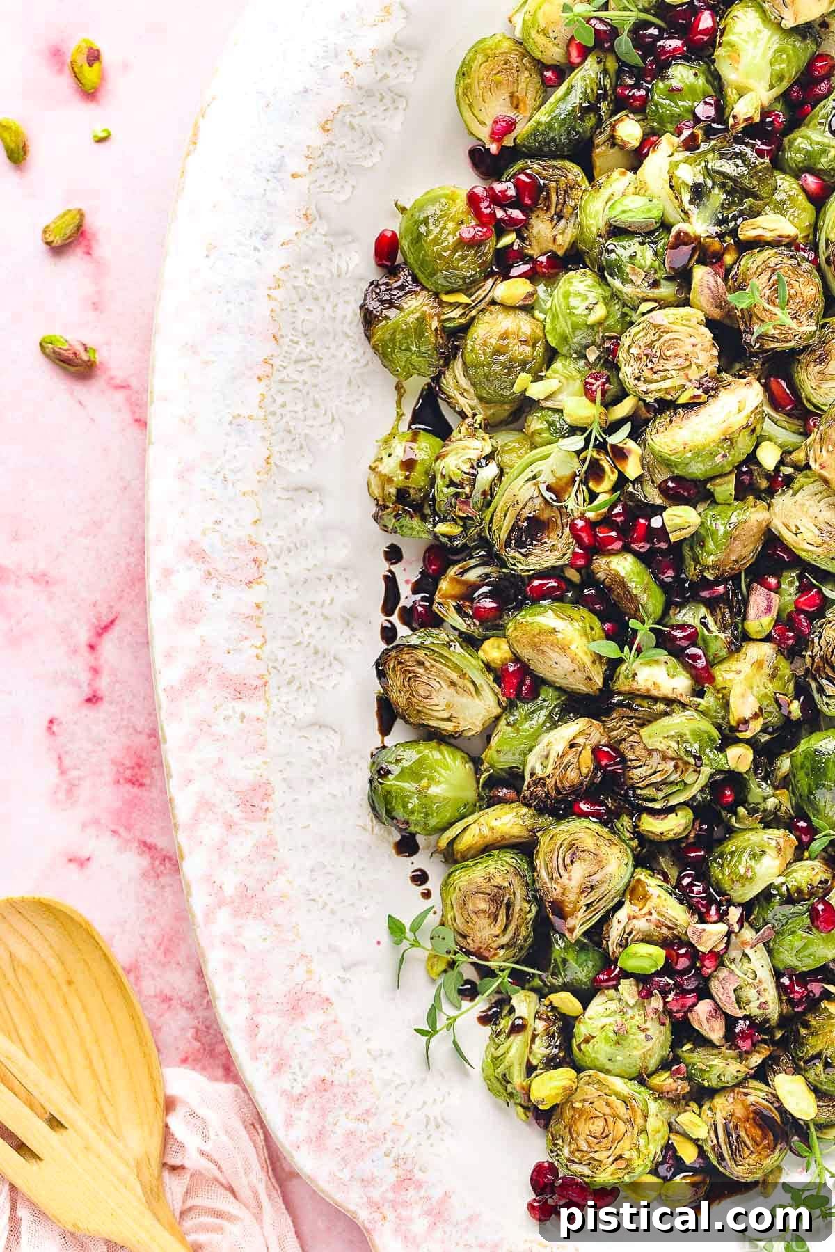 top down view of roasted brussels sprouts on a large white and pink platter. Pomegranate seeds and pistachios garnish the gorgeous dish.