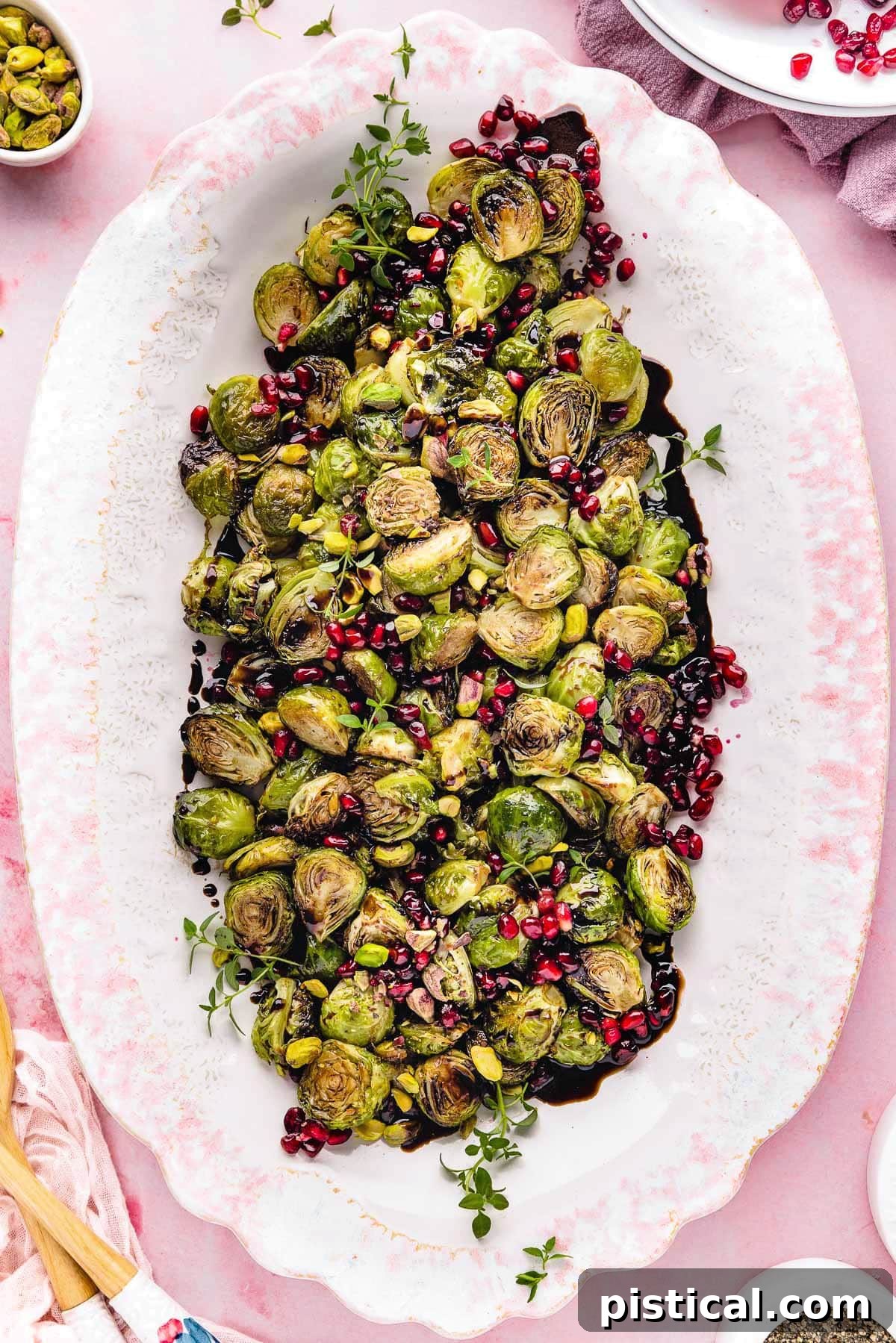 top down view of roasted brussels sprouts on a large white and pink platter. Pomegranate seeds and pistachios garnish the gorgeous dish.