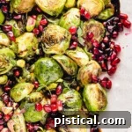 Top down view of roasted brussels sprouts on a pink and white serving dish. the sprouts are topped with pomegranate seeds and thyme along with a balsamic glaze.