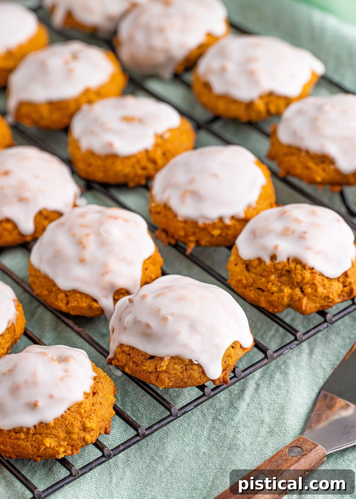 Freshly baked pumpkin oatmeal cookies, generously coated with sweet vanilla icing, neatly arranged on a cooling wire rack.