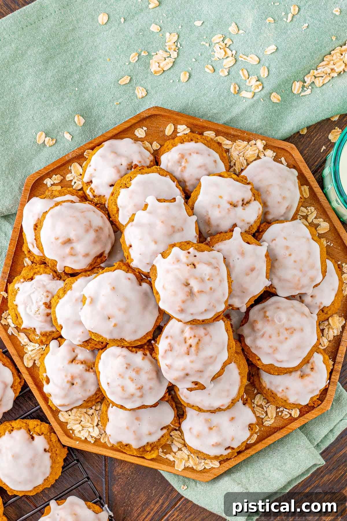 A captivating top-down view of an octagon-shaped wooden tray, abundantly filled with neatly stacked, iced pumpkin oatmeal cookies. A folded green napkin rests gracefully beneath the tray, adding a touch of rustic elegance.