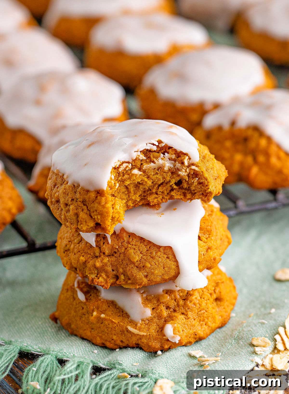 A stack of three irresistible pumpkin cookies, each generously topped with vanilla icing, with the top cookie revealing a delightful bite taken out.