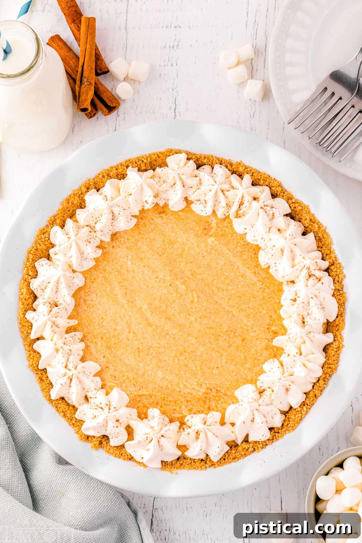 A vibrant, whole no-bake pumpkin pie artfully arranged on a marble surface, adorned with rustic cinnamon sticks and a few stray graham cracker crumbs, hinting at its delicious crust.