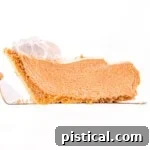 A tantalizing slice of no-bake pumpkin pie being lifted from the pie plate, showcasing its firm, yet creamy filling and golden-brown graham cracker crust.