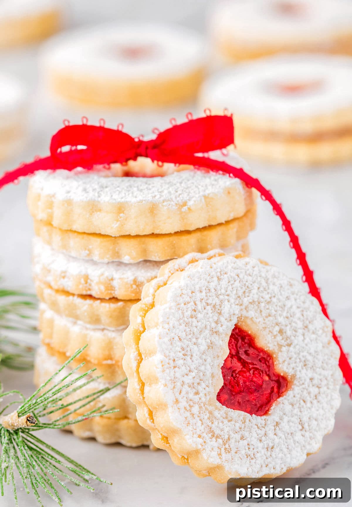 Classic Linzer Cookie Delights 2 stack of linzer cookies with raspberry jam tied with red ribbon. one cookie is leaning up against the stack.