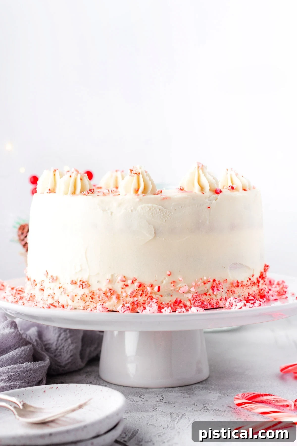 A stunning whole Peppermint Cake stands elegantly on a white cake stand, surrounded by festive candy cane crumbles at its base, ready to be served.