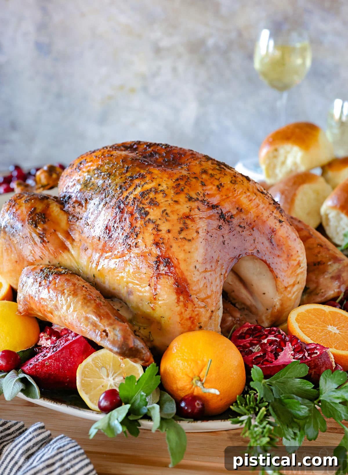 A perfect turkey recipe on a large serving platter, roasted to a golden brown and surrounded by vibrant citrus, fresh herbs, and cranberries. Dinner rolls are visible in the background.