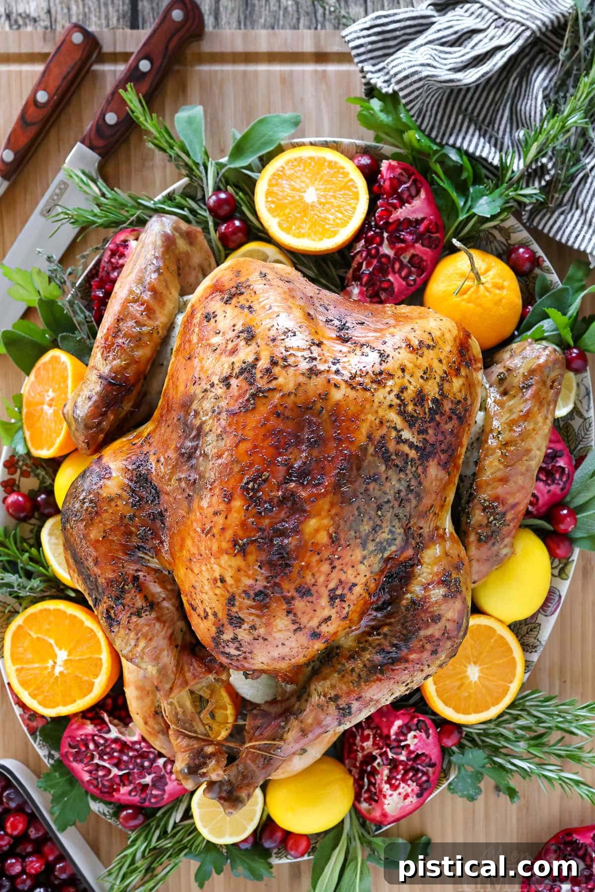 A beautiful top-down view of the best Thanksgiving turkey recipe, presented on a serving platter and garnished with fresh oranges, lemons, pomegranates, herbs, and cranberries.
