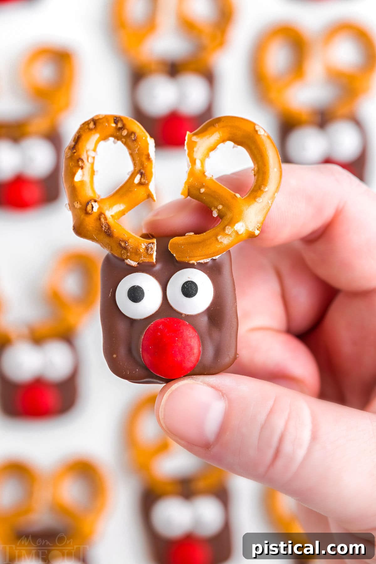 hand holding one of the reindeer pretzels over the rest of the treats setting up on parchment paper.