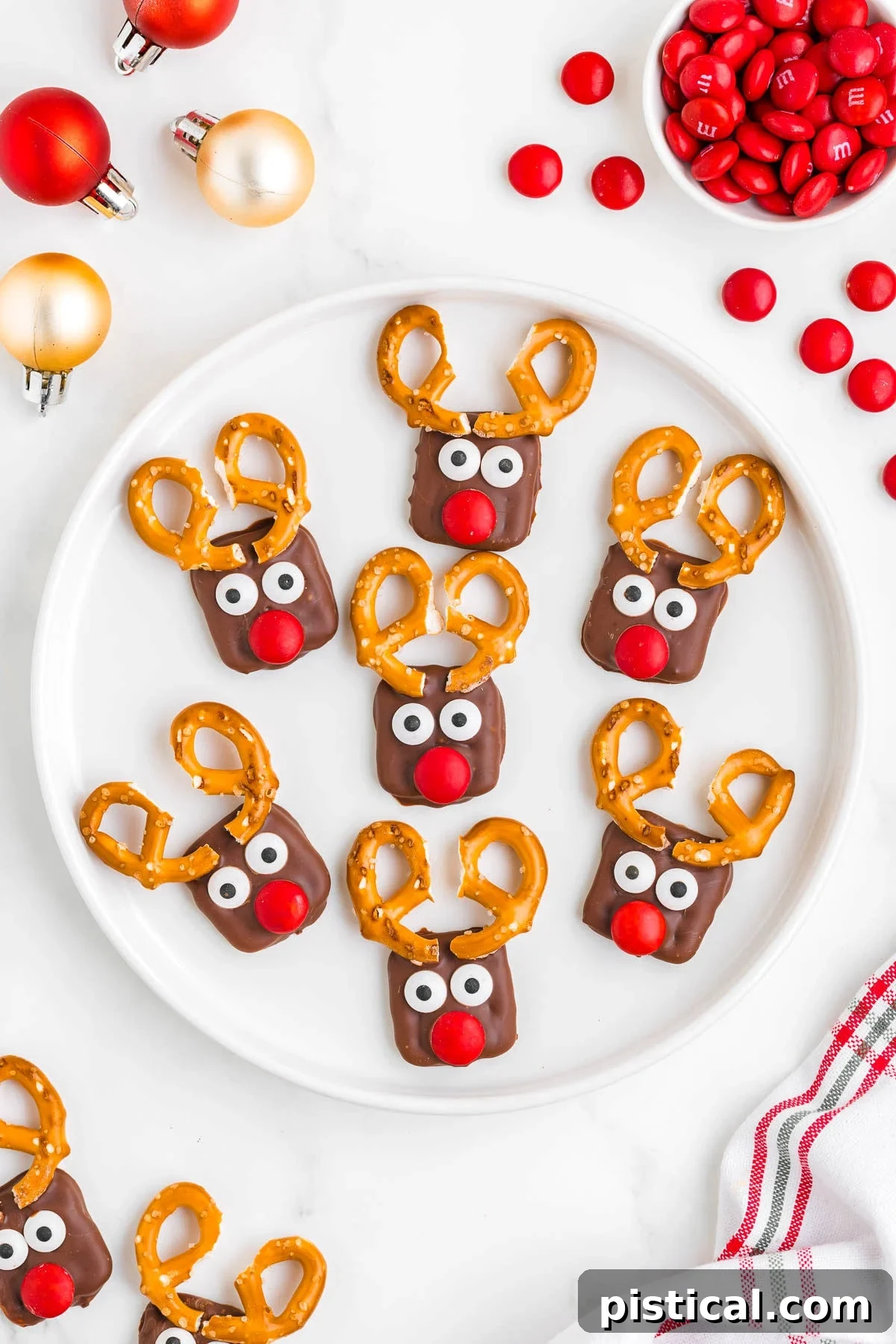 small white plate with seven pretzel reindeer on it surrounded with more treats, candies and ornaments.