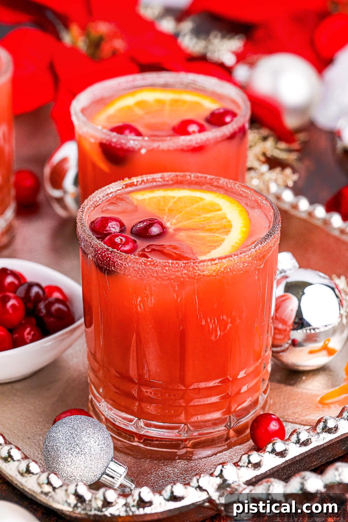 Two vibrant cranberry Christmas cocktails garnished with fresh cranberries and orange slices on a silver serving platter, radiating holiday cheer.