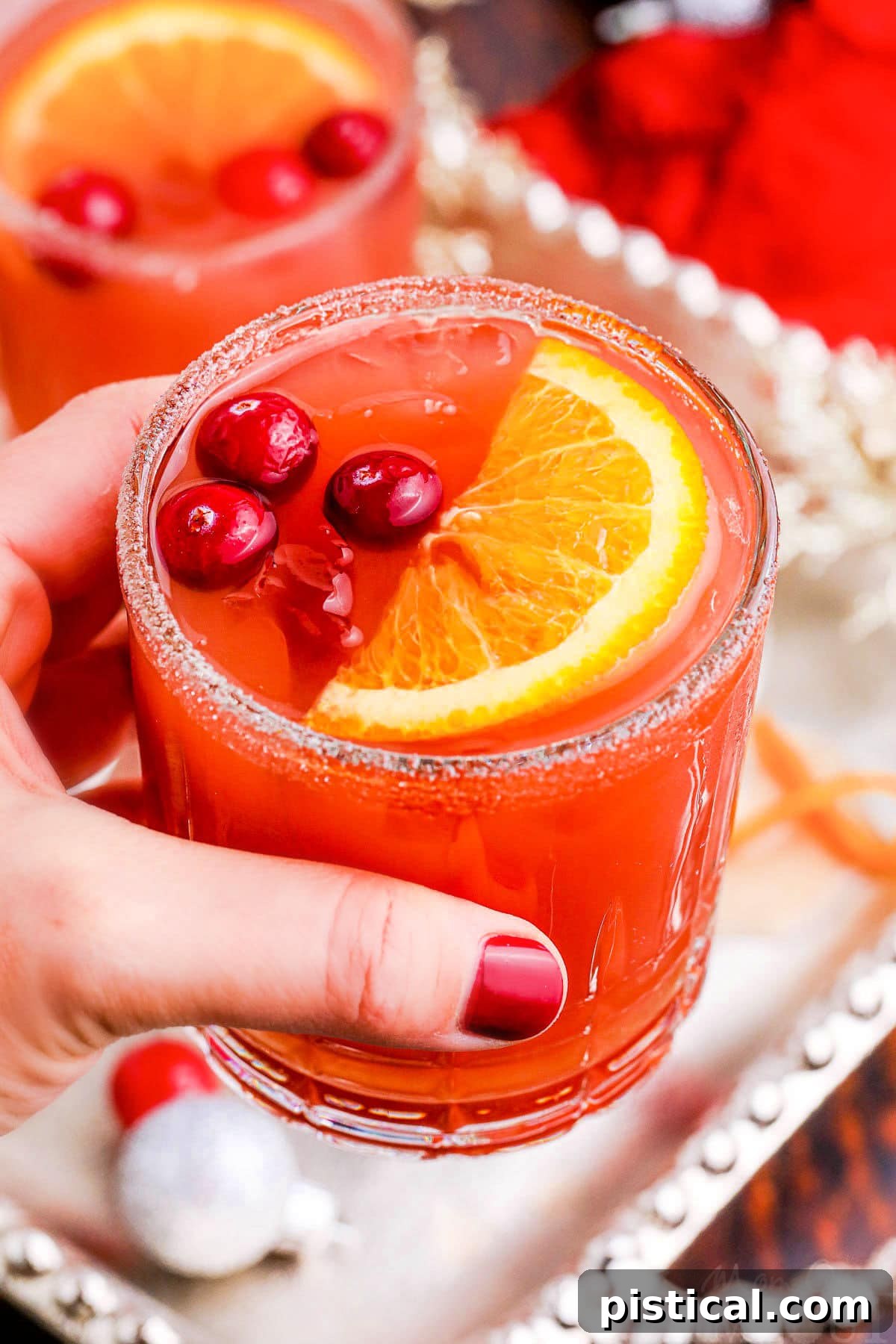 A hand elegantly holding a glass of the festive cranberry Christmas cocktail, highlighting its rich red hue and inviting appeal.