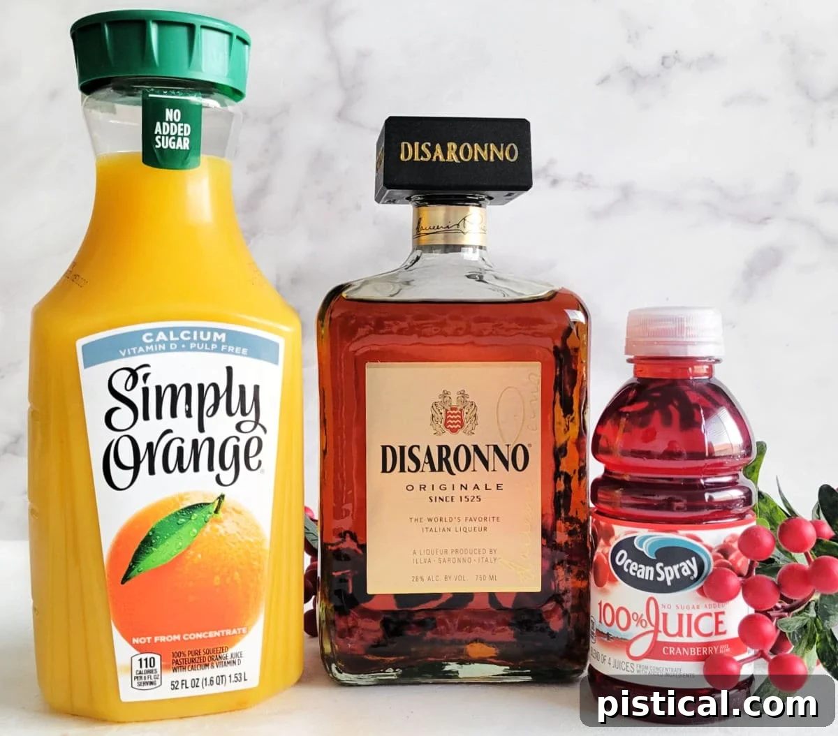 Fresh orange juice, rich amaretto liqueur, and vibrant cranberry juice are neatly arranged on a white surface, ready to be transformed into a delightful Christmas cocktail.
