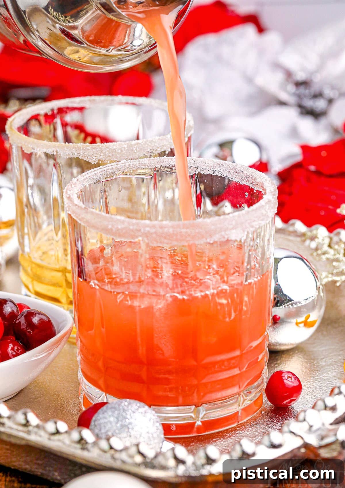 A festive Christmas cocktail being expertly poured into a short, elegant crystal glass resting on a sophisticated silver tray.
