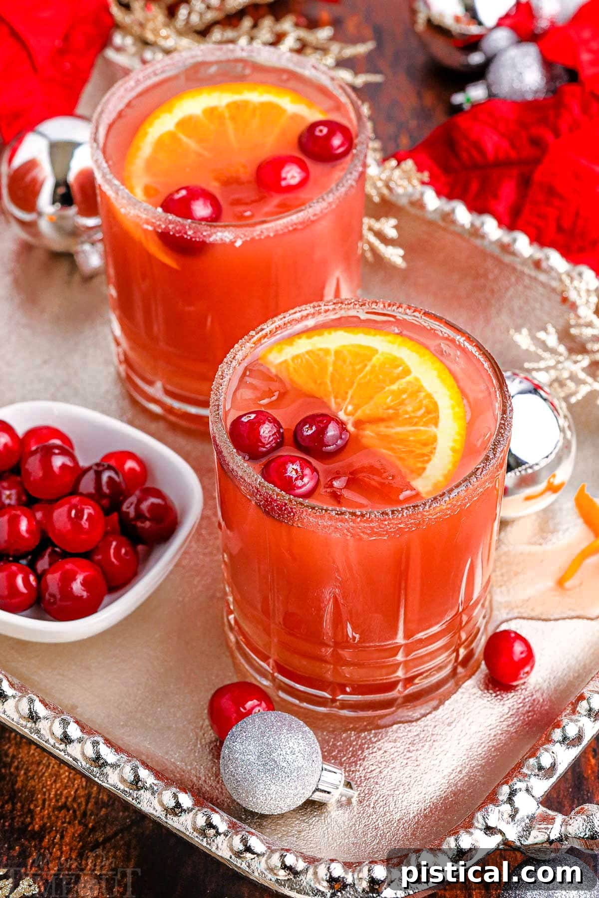 Two identical festive cranberry Christmas cocktails beautifully arranged on a silver serving platter, adorned with fresh cranberries and orange slices.