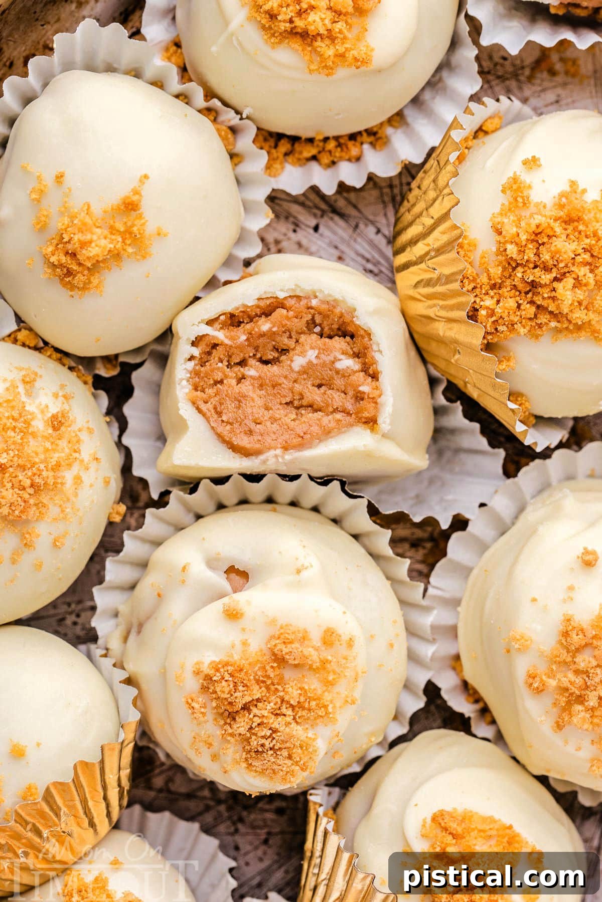 Delightful gingerbread truffles nestled in white paper cups, adorned with gingersnap cookie crumbles and a delicate white chocolate coating. One truffle reveals its delicious interior with a bite taken out.